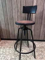 Front view of vintage metal stool showing wooden seat, metal frame, footrest ring, and backrest.