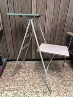Full front and side view of the midcentury folding display stand showing formica top and folding metal legs with cross-supports.