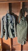 Full view of vintage US Army military jacket and attached duffel bag hanging on wall