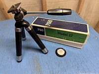 Small Ponder & Best camera tripod model 12 standing with original box and circular level on a blue surface.