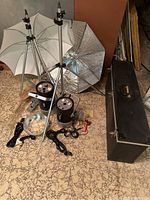 Two Bogen tripods holding umbrella style reflectors (one white, one silver foil) and both Monolite lights on the floor with cords and reflective dome light modifiers. Black carrying case next to the lights.