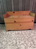 Front view of vintage pine storage bench with hinged lid against wood panel wall and patterned floor.