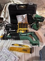 Hitachi cordless drill and reciprocating saw, charger, DeWalt drill blades, drill bit set case, and instruction manuals on white cloth