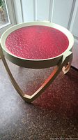 Side view of retro side table showing triangular white plastic base and round red textured plexiglass top.