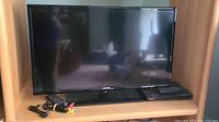 Samsung 45-inch LED TV on wooden cabinet with Sony DVD player below and remotes plus cables in front.