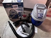 Shop-Vac Hang Up portable wet/dry vacuum unit with black hose, attachments, instruction manual, and original box showing product image and details.