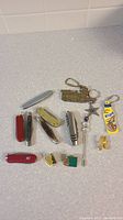 Top-down photo showing all collectible small utility cutting tools, pins, and keychains arranged on a countertop.