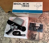 Bolex 150 Super 8 mm camera in original white and blue box with styrofoam insert, camera, strap, and manuals shown.