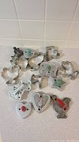 Photo showing assorted vintage metal cookie cutters including elephant, hearts, birds, hand-shaped, and Minnie Mouse, laid out on a white background.