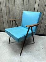 Front angled view of the turquoise vinyl mid-century chair showing wood armrests and metal legs.