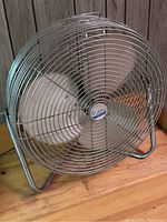 Front view of vintage metal electric stand fan with circular metal grille and four metal blades on a metal stand.