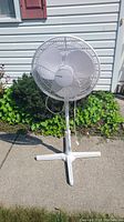 Front view of white Holmes standing fan on pedestal base showing protective grille, blades, and height adjustment pole.