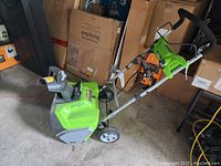 Side angled view showing the full snow blower, green plastic body, wheels, handlebar, and snow chute.