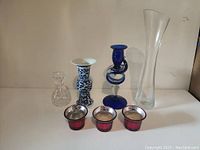 Front view of seven home decor pieces including glass and metal items on a shelf
