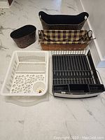 Lot of 5 assorted bins and dish racks including various colors and materials arranged on a white floor.