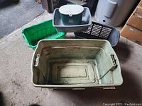 Five assorted plastic storage bins arranged on a concrete floor showing various shapes, sizes, and colors including green, gray, and black, with visible dirt and wear.