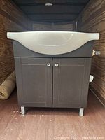 Front view of the dark brown bathroom vanity cabinet base with white ceramic sink basin on top, showing two doors with silver knobs and silver metal legs.