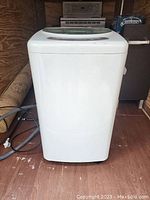 Front view of a white portable washing machine with power and hose visible on floor.