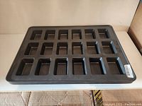 Top-down view of one baking tray showing 24 square compartments and black metal surface with wear.