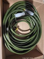 Coiled green garden hose pipe inside a cardboard box, showing entire hose length coiled neatly.