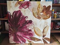 Photo shows a square wrapped canvas painting with large floral imagery in burgundy, rose, gold, and beige tones on an off-white textured background.