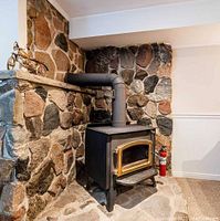 Black metal wood burning stove installed with connected chimney pipe on a stone hearth.