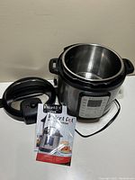 Open Instant Pot Viva pressure cooker with detachable lid beside it, along with two booklets