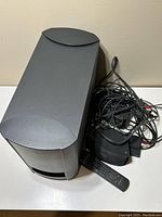 Large black Bose subwoofer speaker with cables and remote control placed together