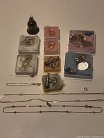 Photo showing Birks bell with cherub on top, various small gold and silver bracelets, and small plastic cases with charms arranged on table.