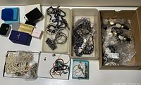 Overview of jewelry lot showing various necklaces, bracelets, earrings, and empty boxes organized in trays and plastic bags.