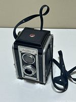 Front and side view of Kodak Duaflex II camera showing lens, brand name and attached strap.