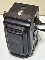 Camera stored in closed brown leather case, silver latch and strap visible