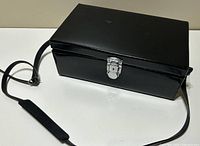 Closed black leather carrying case with shoulder strap and metal clasp on a white surface.