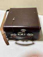 Closed brown leather carrying case with metal latches and shoulder strap