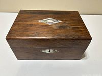 Front top-down view of antique wooden keepsake box showing diamond-shaped mother of pearl inlay on lid and natural wood grain.