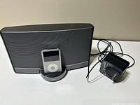 Front view of Bose SoundDock with Apple iPod docked, showing device and power adapter cable and plug.
