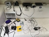 Full overview of lot contents on white surface showing cameras, audio devices, USB drive, photo frames, and cables