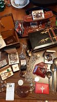 Overview of assorted costume jewelry including rosaries, cufflinks, necklaces, jewelry boxes, and small accessories spread on a table.