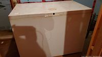 Front view of white chest freezer showing top lid and locking mechanism. The freezer has visible dirt marks on top.
