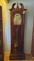Full view of the grandfather clock showing arched top and wood cabinet with glass door
