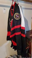 Side view of black Ottawa Senators hockey jersey with red stripes, showing patch on sleeve.