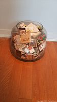 Large clear glass bowl filled with assorted matchboxes and book matches placed on wood floor