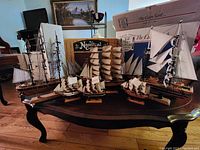 Photo of six model sailing ships arranged on a table in front of nautical-themed decor and boxes.