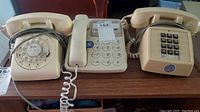 Three vintage telephones on a table including a rotary dial, push button, and GE push button phones