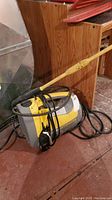Full view of yellow and gray McCulloch pressure jet sprayer with attached black hose and yellow spray wand, placed on floor with wooden background.