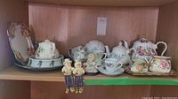 Display shelf with three Sadler ceramic teapots, cream and sugar bowl set, tray, figurines, and teacup