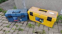 Two plastic tool boxes on outdoor ground, one yellow and one blue, showing exterior and labels