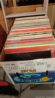 Vinyl records stacked in a white cardboard box showing various album spines and colorful covers