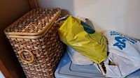Woven laundry hamper with lid next to plastic bin and bags on top of bin