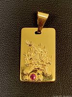 Front view of the rectangular 9K gold pendant showing embossed Chinese dragon and ruby gemstone.